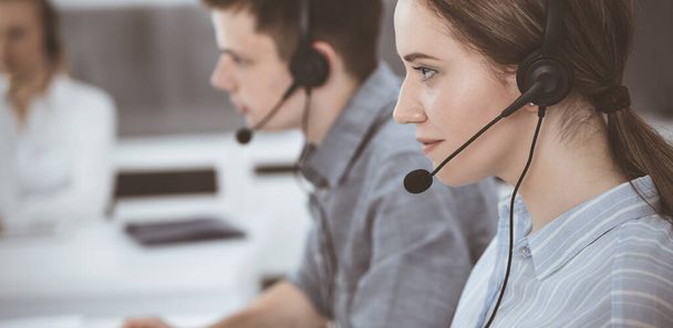 Call center. Group of casual dressed operators at work. Brunette business woman in headset at customer service office - 写真・画像