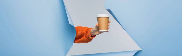 oříznutý pohled na mladou ženu držící papírový šálek s kávou jít na modré roztržené papírové pozadí, banner - Fotografie, Obrázek