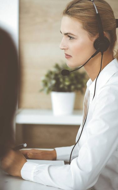Blonde business woman using headset for communication and consulting people at customer service office. Call center - Фото, изображение