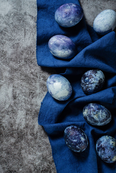 Easter eggs lie on a blue towel on a concrete background. coloring eggs for Easter with natural blueberry juice dye. - Photo, image