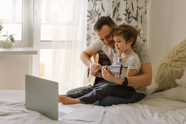 Baba ve oğul online bir derste akustik gitar çalmayı öğrenirler. Oğlumla evde vakit geçirmek, gitar çalmayı öğretmek için. Babalar günün kutlu olsun. - Fotoğraf, Görsel
