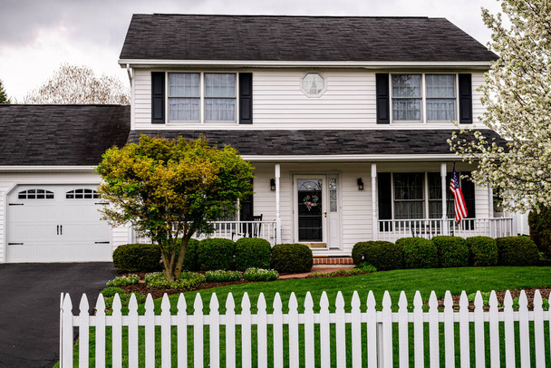 λευκό αποικιακό σπίτι με μαύρα παντζούρια λευκό φράχτη πικετοφορία και αμερικανική σημαία - Φωτογραφία, εικόνα