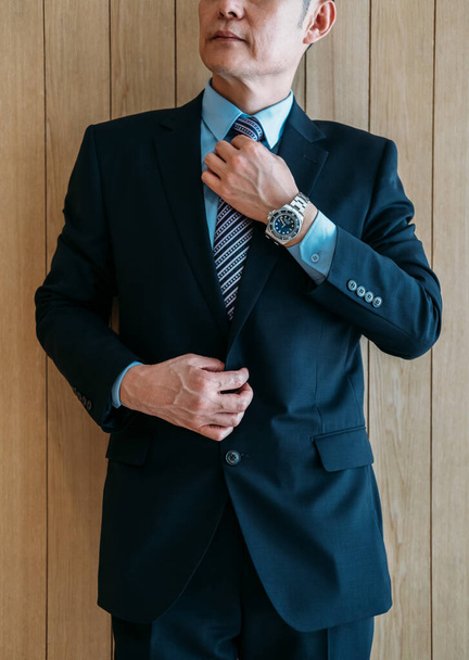 Photo recadrée d'un homme d'affaires ajustant sa cravate dans un bureau avec un mur de planches en bois - Photo, image