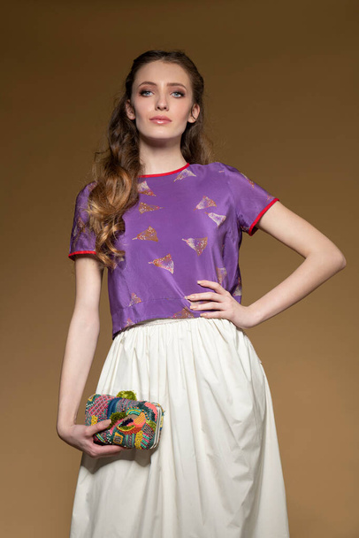 Fashion shot of young woman , she is wearing an elegant summe outfit, with white gown and fuchsia shirt , she keeps a colorful bags  and black shoes  - Photo, Image
