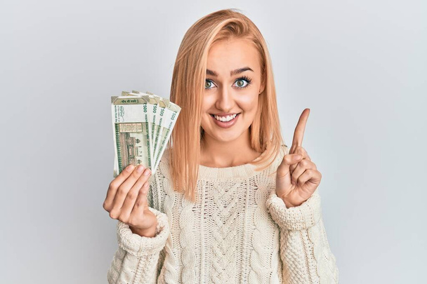 Belle femme caucasienne tenant 500 billets de banque en roupie indienne souriant avec une idée ou une question pointant du doigt avec un visage heureux, numéro un  - Photo, image