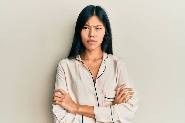 Fiatal kínai nő pizsamában szkeptikus és ideges, rosszalló arckifejezéssel, keresztbe tett karral. negatív személy.  - Fotó, kép