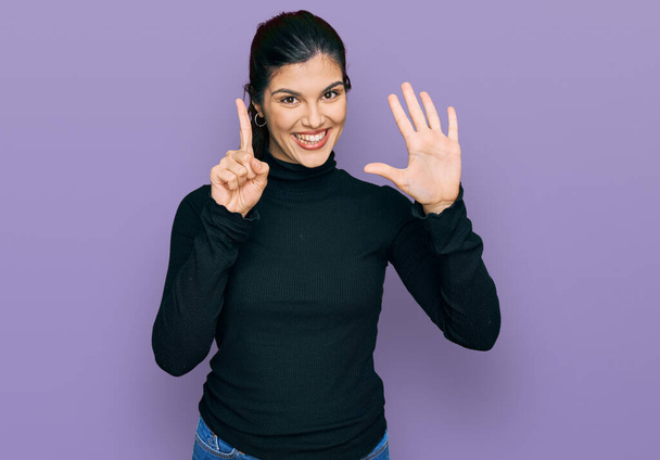 Junge hispanische Frau in lässiger Kleidung zeigt mit Finger Nummer sechs nach oben und lächelt dabei selbstbewusst und glücklich.  - Foto, Bild