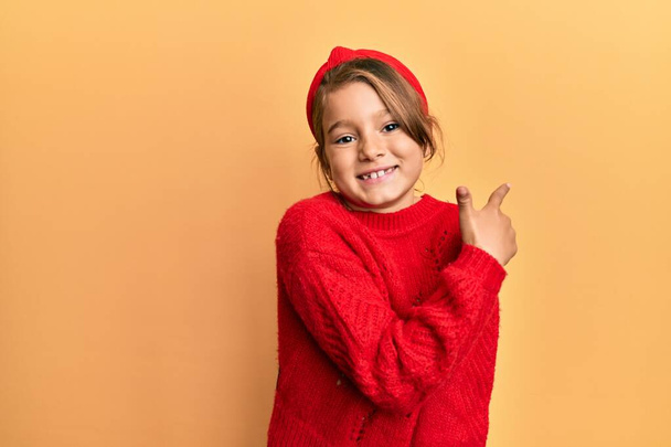 Μικρό όμορφο κορίτσι φορώντας casual πουλόβερ χειμώνα χαμογελώντας χαρούμενα δείχνοντας με το χέρι και το δάχτυλο μέχρι το πλάι  - Φωτογραφία, εικόνα