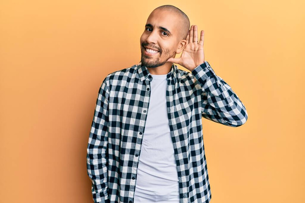 Hombre adulto hispano usando ropa casual sonriendo con la mano sobre el oído escuchando y escuchando rumores o chismes. concepto de sordera.  - Foto, imagen