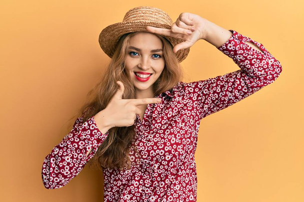 Yazlık şapkalı güzel sarışın kadın gülümsüyor. Elleriyle ve parmaklarıyla gülen yüzüyle çerçeve yapıyor. yaratıcılık ve fotoğrafçılık kavramı.  - Fotoğraf, Görsel