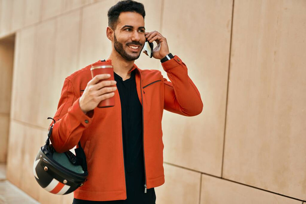 Joven hispano hablando en el smartphone tomando café en la ciudad. - Foto, imagen
