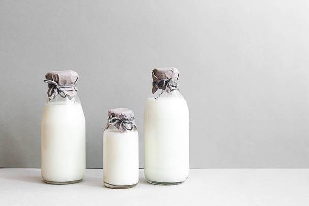 Minimale stilstand van melkflessen op een lichte achtergrond met kopieerruimte. Zuivelproductie, biologisch product. Het concept van gezond eten en een duurzame levensstijl. - Foto, afbeelding