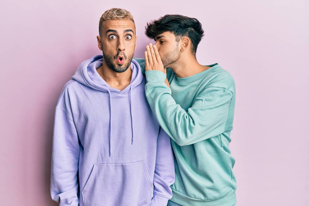 Homosexual gay couple standing together wearing casual clothes hand on mouth telling secret rumor, whispering malicious talk conversation  - Photo, Image