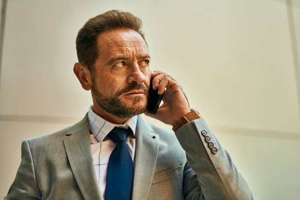 Geschäftsmann mittleren Alters mit ernstem Gesichtsausdruck spricht auf dem Smartphone in der Stadt. - Foto, Bild