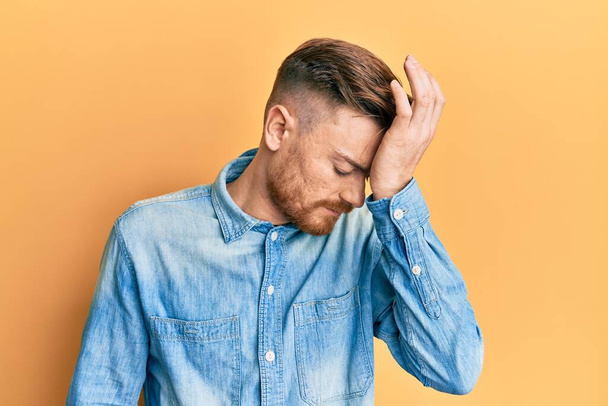 Young redhead man wearing casual denim shirt surprised with hand on head for mistake, remember error. forgot, bad memory concept.  - Photo, Image