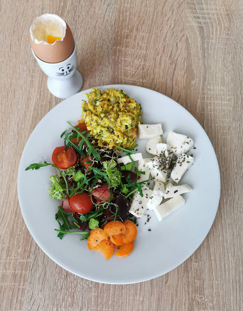 Gezond voedsel - zacht gekookt ei, biologische tomaten- en groentesalade, broccoli, wortel, rucolabladeren, mozzarella kaas - Foto, afbeelding