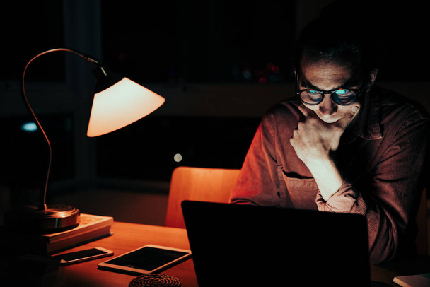 zmęczony kaukaski mężczyzna freelancer sortowanie przez zdjęcia na laptopie pracuje do późna w nocy w domu biuro - Zdjęcie, obraz