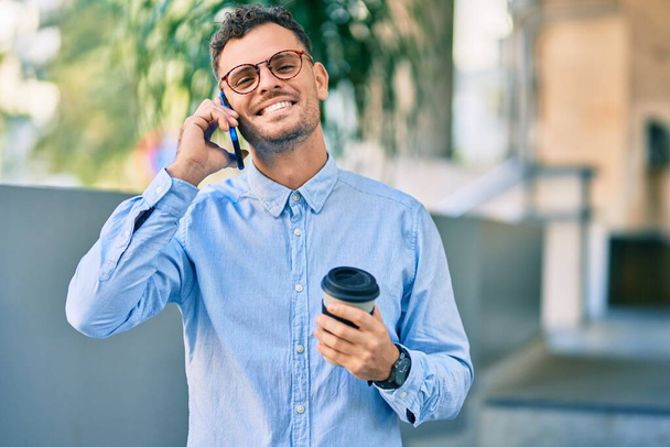 Nuori latino liikemies puhuu älypuhelimella ja juo kahvia kaupungissa. - Valokuva, kuva