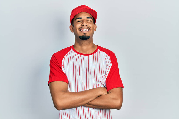 野球の制服を着た若いアフリカ系アメリカ人の男が驚きのために口を開けて驚いて、不信の顔  - 写真・画像