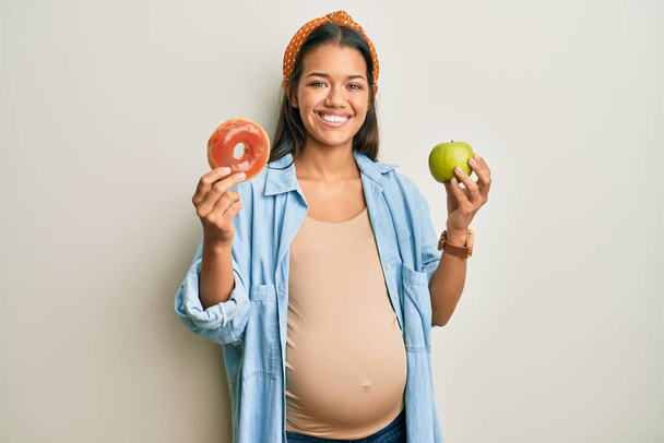 Mulher hispânica bonita esperando um bebê, segurando comida sorrindo com um sorriso feliz e legal no rosto. mostrando dentes.  - Foto, Imagem