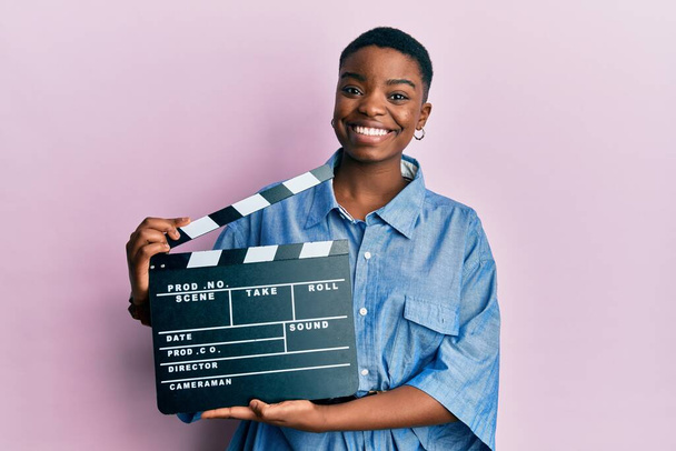 Genç Afro-Amerikan kadın elinde video film panosu, yüzünde mutlu ve havalı bir gülümsemeyle gülümsüyor. diş gösterme.  - Fotoğraf, Görsel