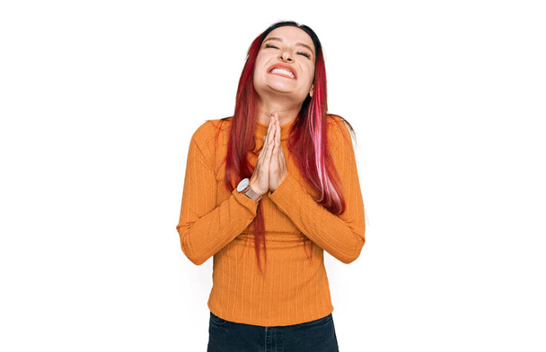 Молода біла жінка в повсякденному одязі молиться і молиться разом з надією висловлюватися на обличчі дуже емоційно і стурбовано. благання
.  - Фото, зображення