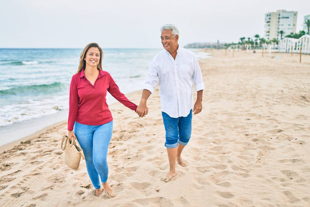 Couple hispanique moyen âge souriant heureux marchant sur la plage. - Photo, image