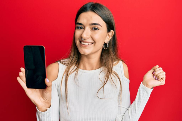 Young hispanic woman holding smartphone showing blank screen screaming proud, celebrating victory and success very excited with raised arm  - Foto, immagini