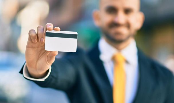 Młody Latynos łysy biznesmen uśmiechnięty szczęśliwy trzymając kartę kredytową w mieście. - Zdjęcie, obraz