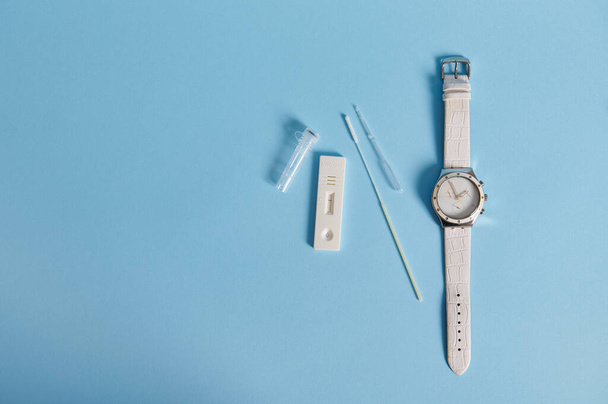 Flat lay composition of a covid-19 rapid antigen test and hand watches isolated on blue background with copy space - Foto, afbeelding