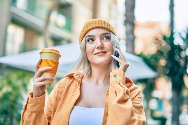 Jeune fille blonde parlant sur le smartphone boire du café à la ville. - Photo, image