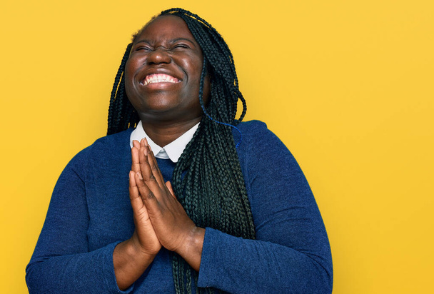 Jonge zwarte vrouw met vlechten in casual kleding bedelen en bidden met de handen samen met hoop uitdrukking op het gezicht zeer emotioneel en bezorgd. bedelen.  - Foto, afbeelding
