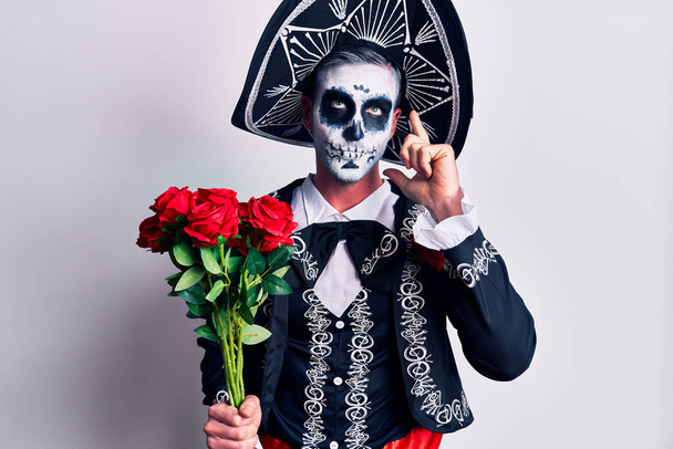 Fiatalember visel mexikói nap a halott jelmez gazdaság virágok komoly arc gondolkodás kérdés kézzel az állon, gondolkodó zavaros ötlet  - Fotó, kép