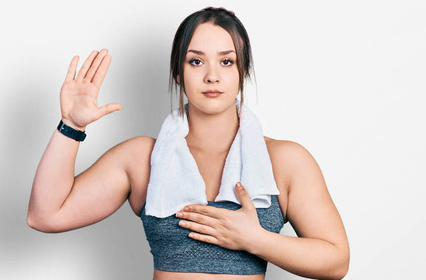 Young hispanic girl wearing sportswear and towel swearing with hand on chest and open palm, making a loyalty promise oath  - Photo, Image