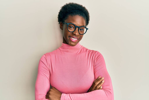 Jong Afrikaans-Amerikaans meisje met casual kleren en een bril vrolijk gezicht glimlachend met gekruiste armen kijkend naar de camera. positieve persoon.  - Foto, afbeelding