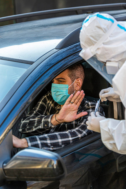 Man refuses medical worker trying to perform drive-thru COVID-19 test, taking nasal swab sample from patient through car window, PCR diagnostic, doctor in PPE holding test kit.  - Photo, Image