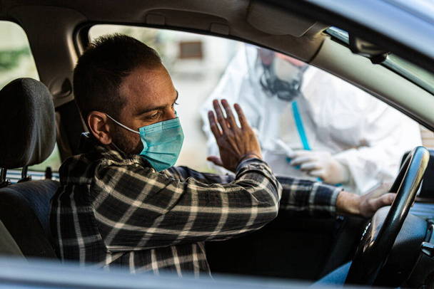 Man refuses medical worker trying to perform drive-thru COVID-19 test, taking nasal swab sample from patient through car window, PCR diagnostic, doctor in PPE holding test kit. - Foto, imagen