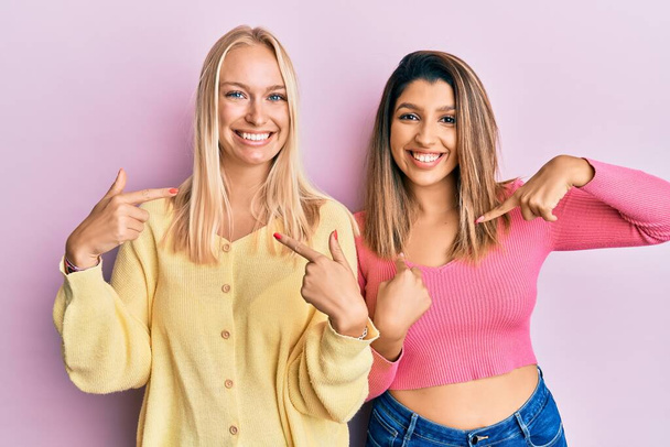 Dois amigos juntos sobre fundo rosa olhando confiante com sorriso no rosto, apontando-se com os dedos orgulhosos e felizes.  - Foto, Imagem