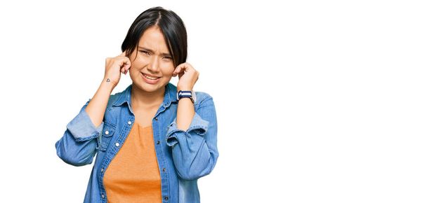 Jonge mooie Spaanse vrouw met kort haar in casual spijkerjasje over oren met vingers met geïrriteerde uitdrukking voor het lawaai van luide muziek. doof concept.  - Foto, afbeelding