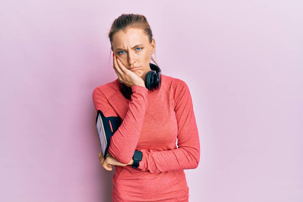 Beautiful caucasian woman wearing sportswear and arm band thinking looking tired and bored with depression problems with crossed arms.  - 写真・画像