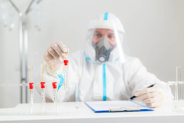 Trabajador médico en PPE que trabaja con la prueba COVID-19 en el laboratorio del hospital, anotando los resultados. - Foto, imagen