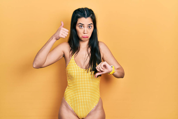 Young hispanic girl wearing swimsuit doing thumbs up and down, disagreement and agreement expression. crazy conflict  - Foto, afbeelding
