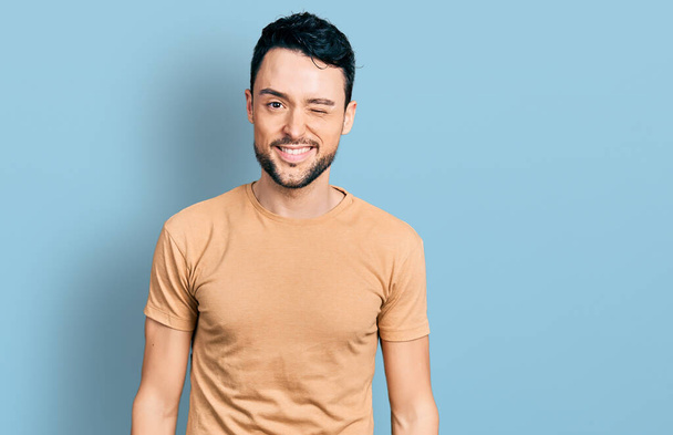 Homme hispanique avec barbe portant t-shirt décontracté cligner des yeux en regardant la caméra avec une expression sexy, gai et heureux visage.  - Photo, image