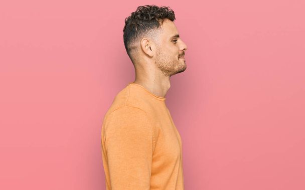 Jeune homme hispanique portant des vêtements décontractés regardant vers le côté, pose de profil relax avec le visage naturel avec sourire confiant.  - Photo, image