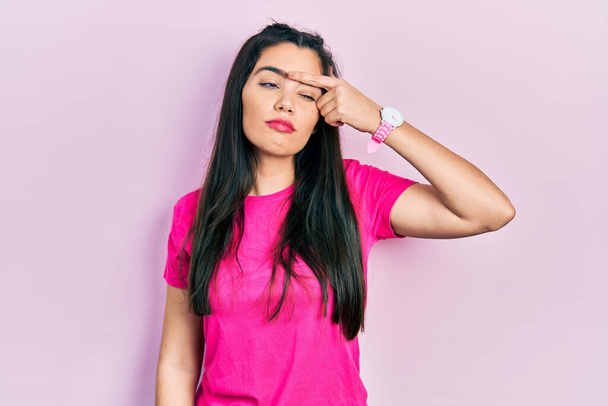 Jong Latijns-Amerikaans meisje draagt casual roze t-shirt wijzend ongelukkig te pukkelen op het voorhoofd, lelijke infectie van blackhead. acne en huidprobleem  - Foto, afbeelding