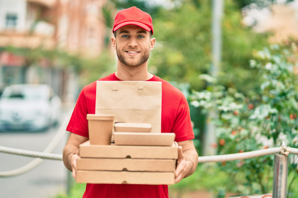 Young caucasian deliveryman smiling happy holding delivery food at the city. - Foto, afbeelding