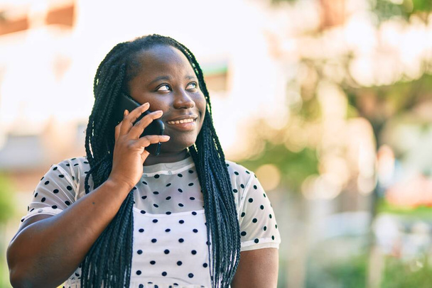 Молодая африканская американка улыбается счастливо разговаривая по смартфону в городе. - Фото, изображение