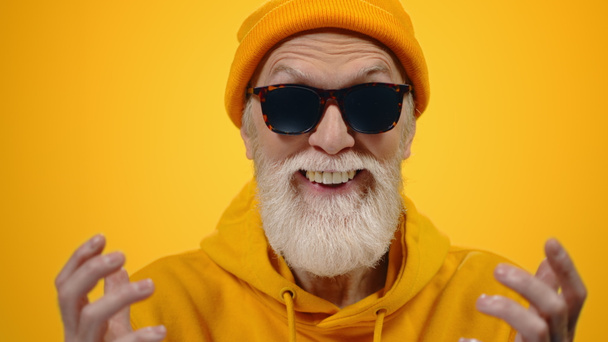 Old man having fun indoor. Joyful guy gesticulating on yellow studio background. - Foto, afbeelding