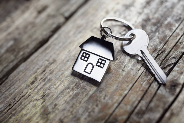 House key on a house shaped keychain resting on wooden floorboards concept for real estate, moving home or renting property - Foto, Imagen