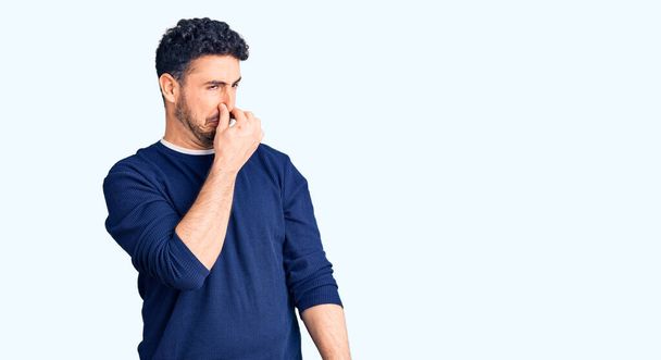 Jeune homme hispanique portant des vêtements décontractés sentant quelque chose de puant et dégoûtant, odeur intolérable, retenant son souffle avec les doigts sur le nez. mauvaise odeur  - Photo, image